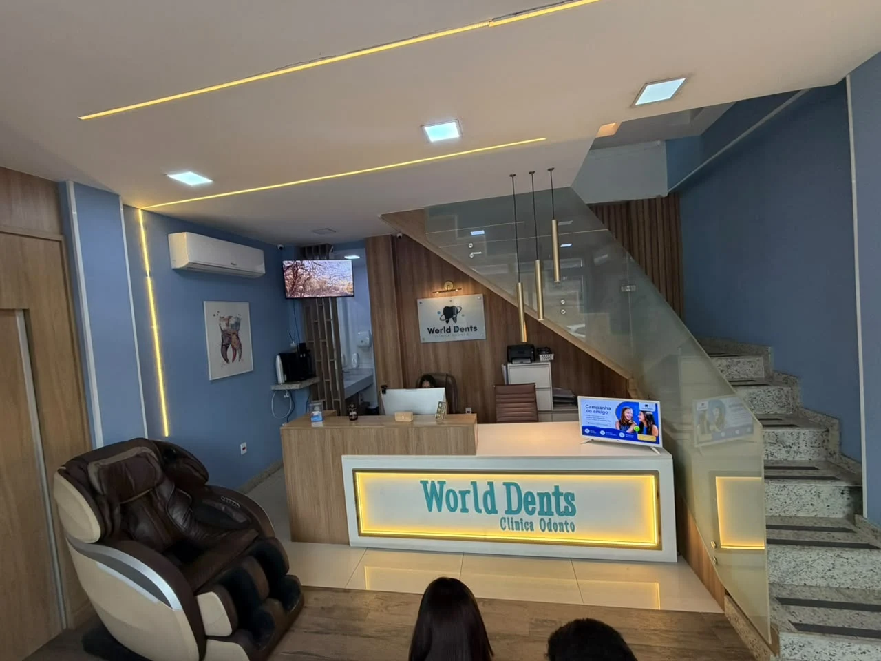 Recepção da World Dents com cadeira de massagem, balcão iluminado e escada